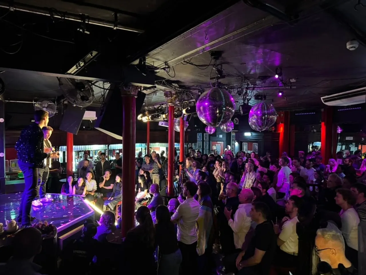 A packed audience watches Elephant in the Room at the Royal Vauxhall Tavern, with the hosts on stage beneath disco balls.
